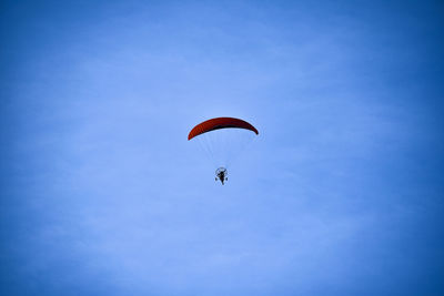 Low angle view of person paragliding against blue sky