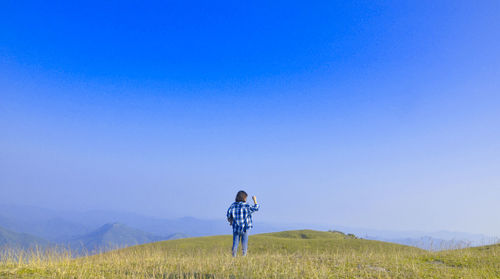 Person standing on field against clear blue sky during sunny day