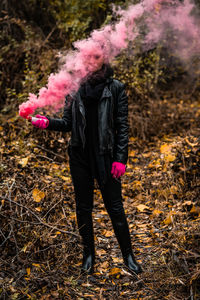 Young woman holding distress flare while standing in forest during autumn