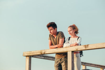 Low angle view of couple looking away while standing by railing against clear sky