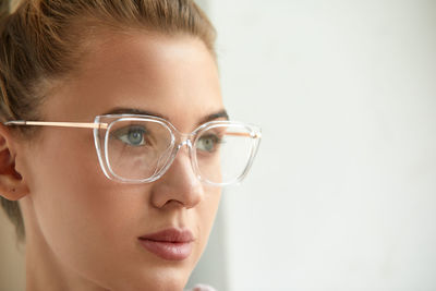 Close-up of young woman wearing eyeglasses against white background