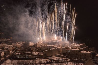 Firework display over houses against sky at night