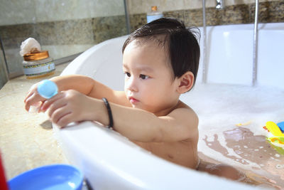 Cute baby boy sitting in bathtub in bathroom