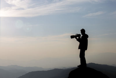 Silhouette man photographing on mountain against sky during sunset