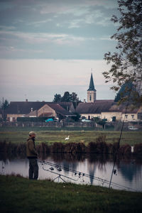 Side view of man fishing by lake against church