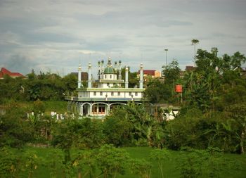 Built structure by trees and plants against sky