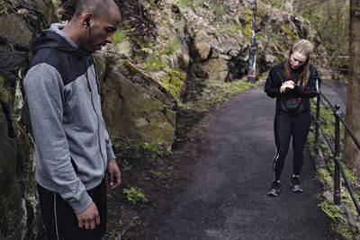 Side view of tired male athlete standing on road with woman in background