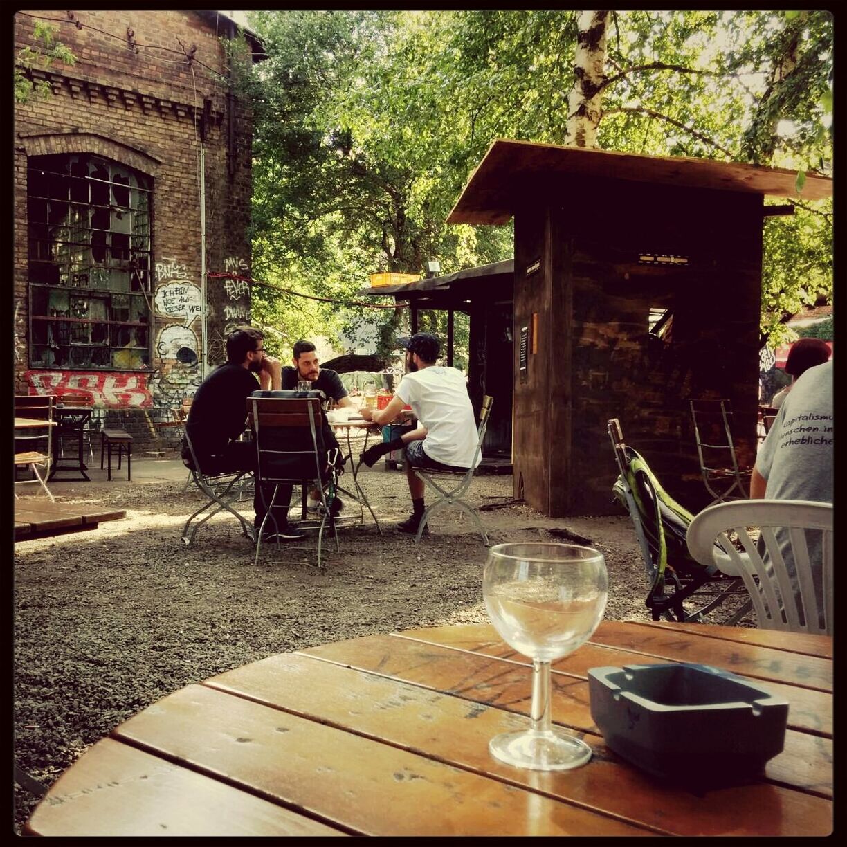 transfer print, men, sitting, lifestyles, building exterior, person, chair, table, built structure, architecture, auto post production filter, sidewalk cafe, leisure activity, rear view, medium group of people, full length, day, tree