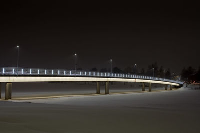 Bridge over illuminated street against clear sky at night