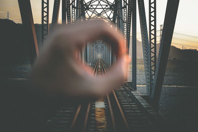 Railway bridge seen through hole made from hand against sky during sunset