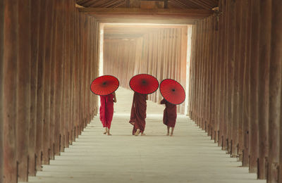 Rear view of monks with paper umbrella walking on walkway of pagoda