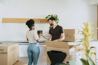 Multiracial couple unpacking bowls from cardboard box in kitchen at new home