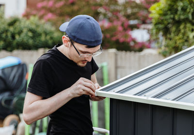 One young guy with his own hands screws a screw into the plugs of the roof of a metal barn.