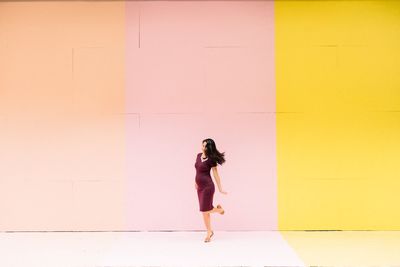 Full length of young woman standing against yellow wall