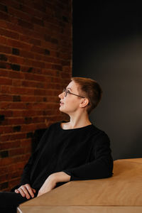 Young woman with short hair in eyeglasses and black sweater sitting at the table in office