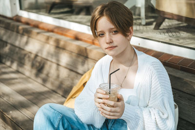 A trendy teenage girl, exuding cool vibes, leisurely sips on iced coffee