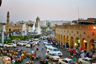 Vehicles and people on street in city against sky