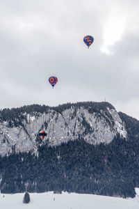 Hot air ballon flying over snow covered mountain against sky