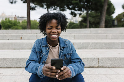Smiling young man using mobile phone while sitting on staircase