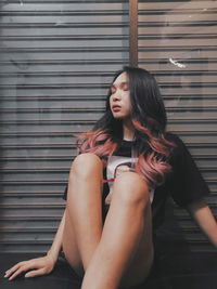 Beautiful young woman sitting against wall