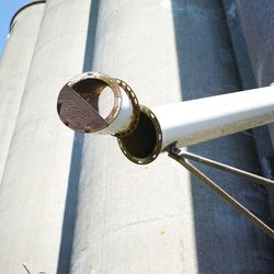 Low angle view of metallic pipe against silos during sunny day