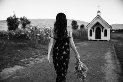 Woman walking towards tiny chapel with flowers in hand