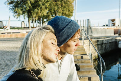 Young couple with eyes closed relaxing at harbor during sunny day