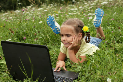 Young woman using laptop while sitting on field