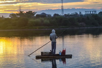 Man fishing in lake against sky during sunset