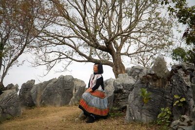 Woman sitting on rock against tree