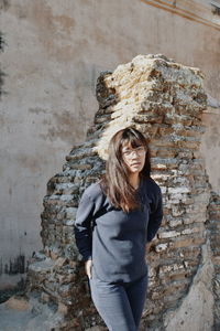 Portrait of young woman standing against weathered wall