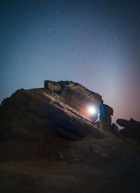 Anonymous tourist standing with illuminated torch on stone in mountains on background of starry sky at night