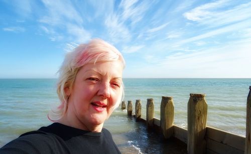 Close-up portrait of mature woman standing at beach against sky