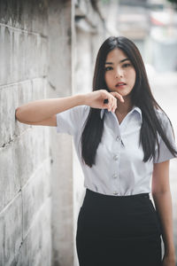 Portrait of a young woman standing against wall