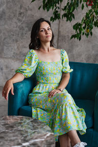 Portrait of young woman sitting against wall