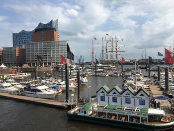 Sailboats moored on harbor by buildings in city against sky