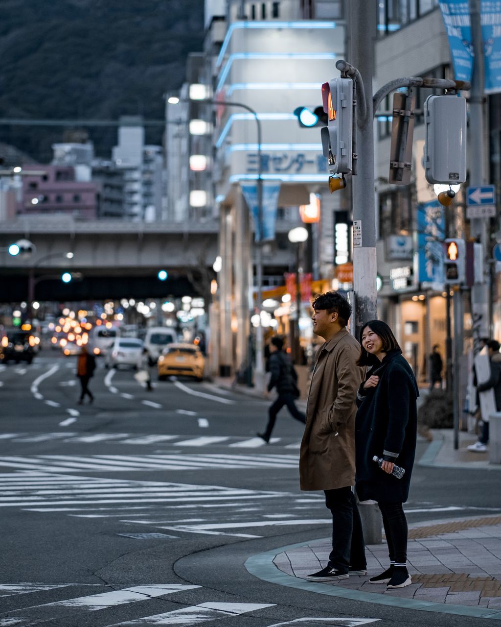 city, two people, architecture, building exterior, street, real people, transportation, city life, walking, road, road marking, full length, incidental people, women, built structure, men, crossing, illuminated, sign, adult, city street, light, outdoors, couple - relationship