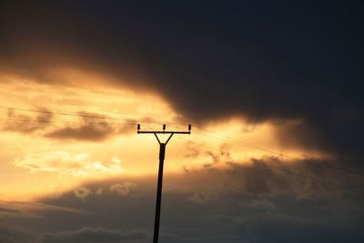 Low angle view of silhouette telephone pole against cloudy sky during sunset