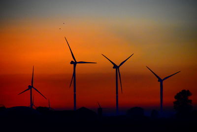 Silhouette wind turbines on field against sky during sunset