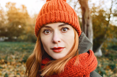 Bright cute young woman in orange warm knitted hat and scarf. autumn portrait close-up.