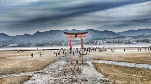 Group of people at beach against cloudy sky