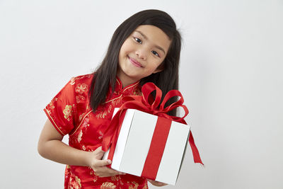 Portrait of smiling girl holding gift box against white background