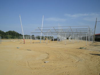 Metallic construction frames on sand against blue sky during sunny day