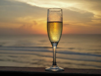 Close-up of beer glass on table against sea during sunset