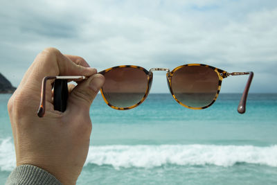 Cropped hand holding sunglasses against horizon
