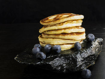 Close-up of stacked pancakes with blueberries on black stone at table