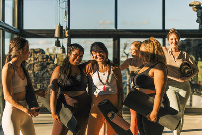 Portrait of happy female friends standing together holding exercise mats after yoga class