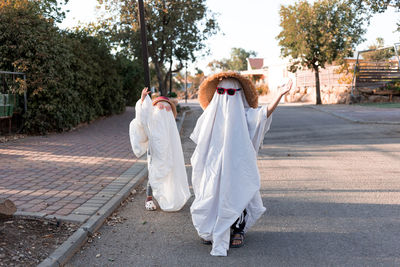 Trendy sheet ghosts costumes on little kids standing on a suburbs street. happy halloween holiday