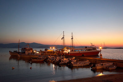 Boats moored in harbor at sunset