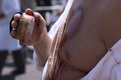 Midsection of man with injured body holding sharp equipment during religious event